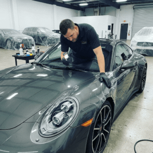 Man inspecting a gray car with a flashlight.